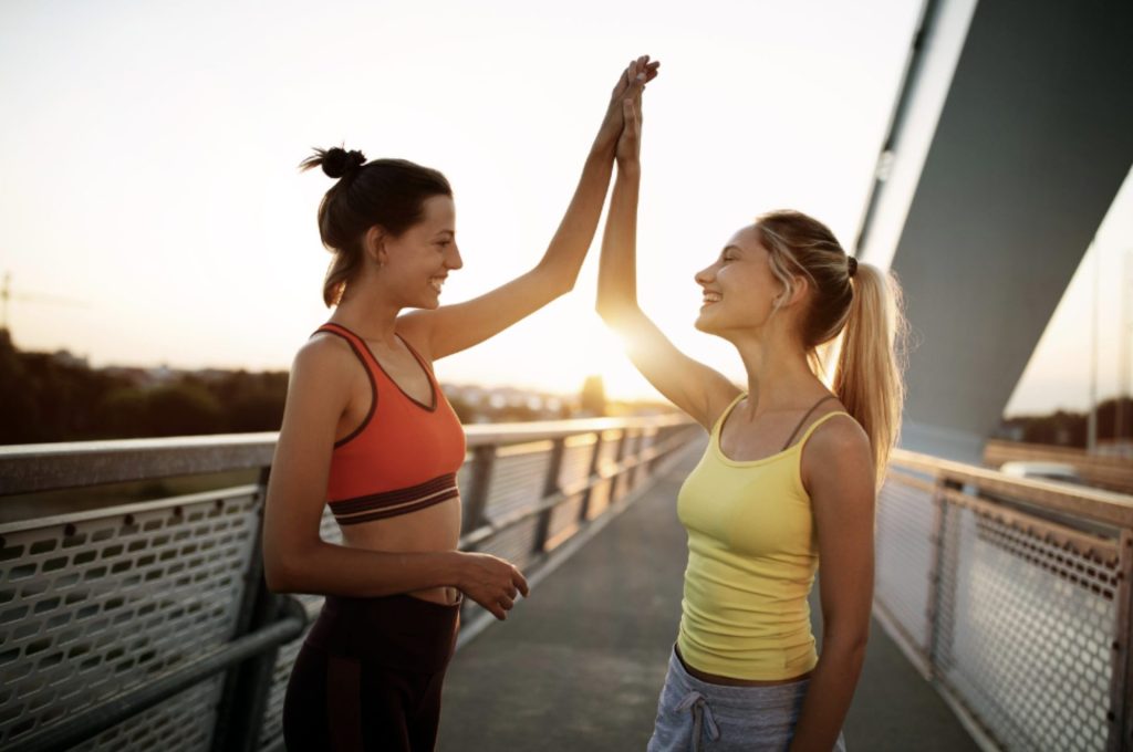 Fitness trainer nutritionist and her student high-fiving on bridge after a successful training session.